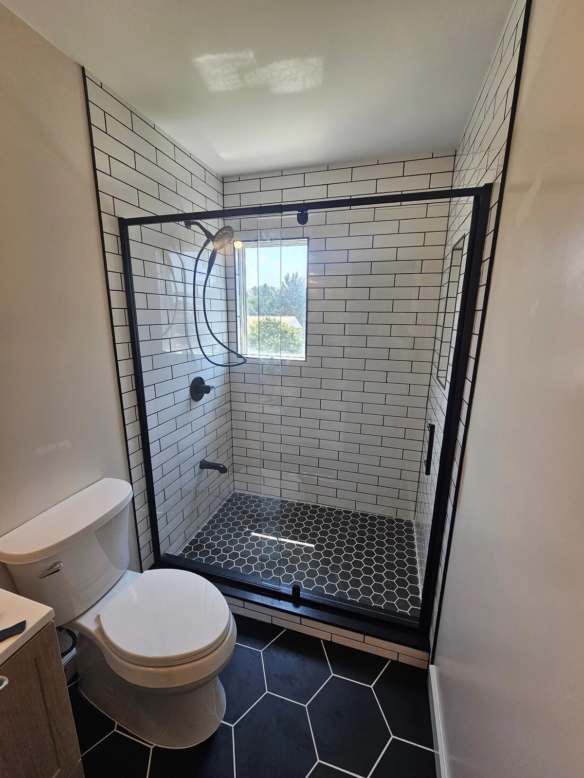 Finished Newburgh bathroom remodel with walk-in subway tile shower, black framed glass door, and black hex tile floor