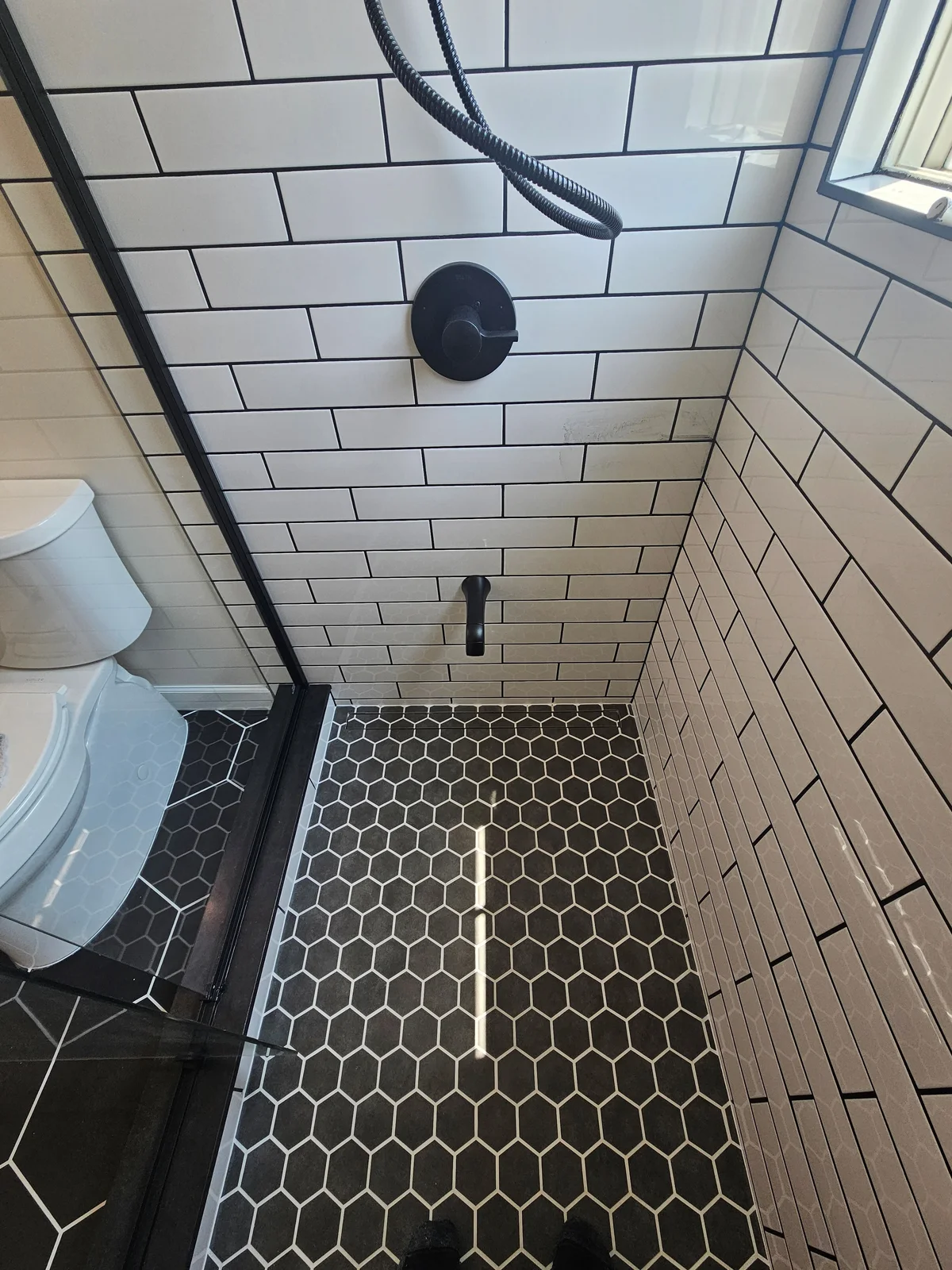 Finished Newburgh bathroom remodel with walk-in subway tile shower, black framed glass door, and black hex tile floor - photo 1