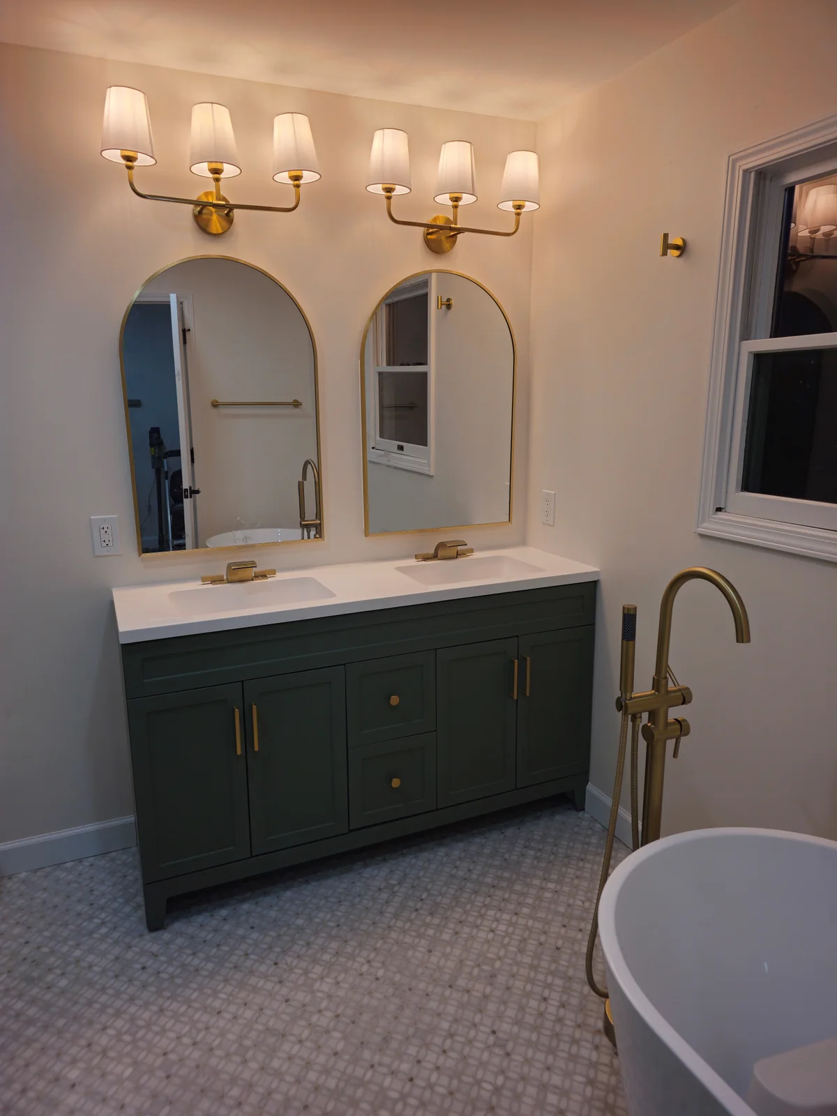 Finished Evansville bathroom remodel with dark green double vanity, arched mirrors, brass sconces, and freestanding tub