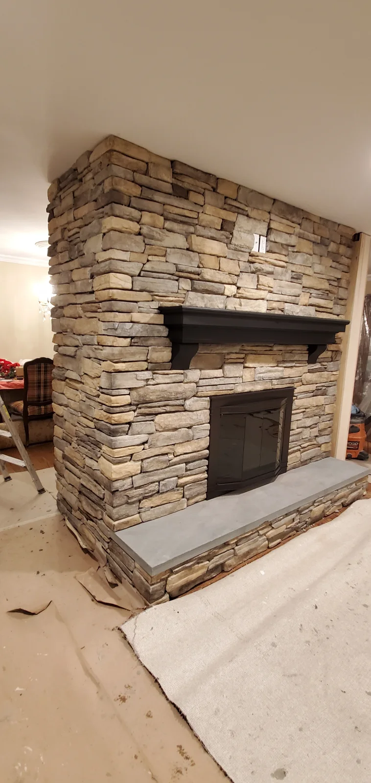 Finished Newburgh stone veneer fireplace with stacked stone surround, dark mantel, and raised hearth