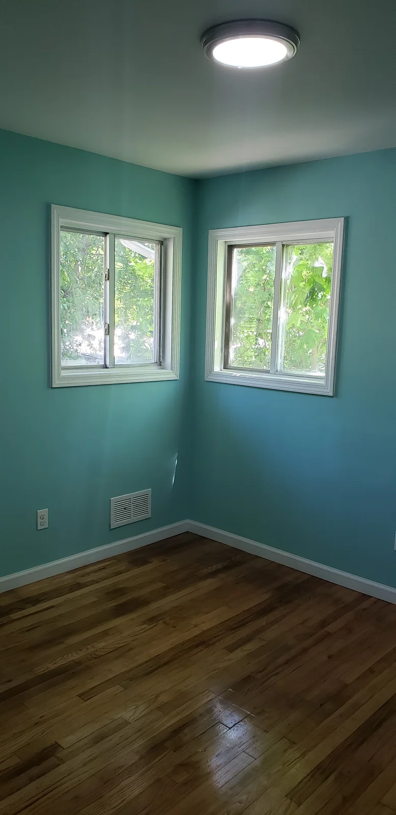 Finished rental property living room with teal walls, white trim, black entry door, large window, and refinished hardwood floor - photo 1