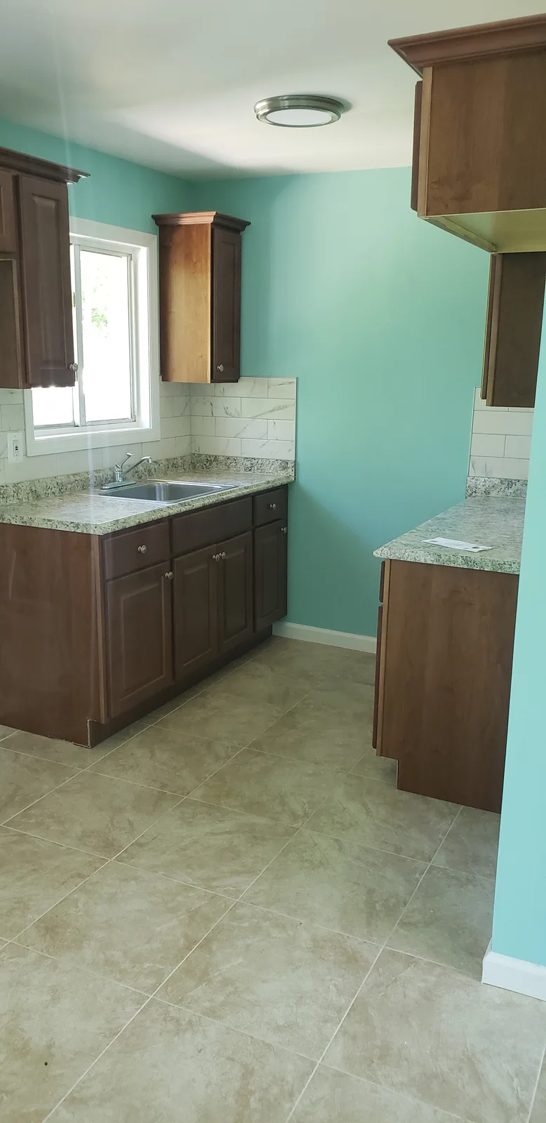 Finished rental property living room with teal walls, white trim, black entry door, large window, and refinished hardwood floor - photo 2
