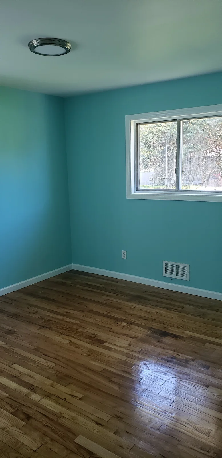 Finished rental property living room with teal walls, white trim, black entry door, large window, and refinished hardwood floor - photo 4