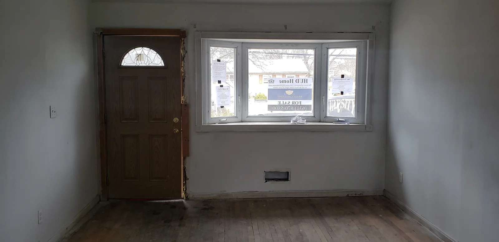 Finished rental property living room with teal walls, white trim, black entry door, large window, and refinished hardwood floor - photo 5